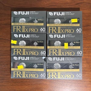 Könnte beinhalten: Sechs FUJI FR-IIx PRO 60 Audiokassetten. Jede Kassette befindet sich in einer schwarz-silbernen Box mit dem FUJI-Logo und dem Text "Resists Heat and Vibration for Superior Sound Quality".