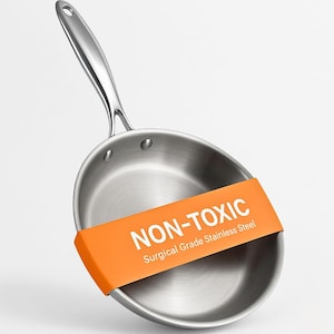 May include: Stainless steel frying pan with a long handle. The pan has a silver finish and an orange band that reads "NON-TOXIC Surgical Grade Stainless Steel". The pan is designed for cooking.