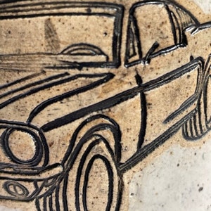 May include: A black and white illustration of a classic car on a beige background. The car has a rounded front end, a large windshield, and a detailed tire design.