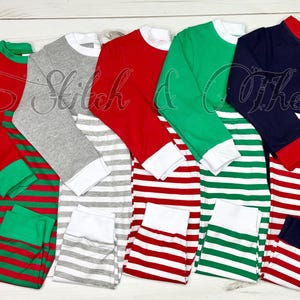 May include: Five pairs of striped pajamas in red, green, gray, and navy blue with white stripes. The pajamas have long sleeves and a crew neck.