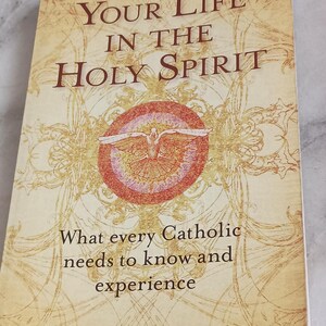 May include: Book cover with a yellow background and a red circle with a dove inside. The title is "Your Life in the Holy Spirit" and the subtitle is "What every Catholic needs to know and experience". The author is Alan Schreck.