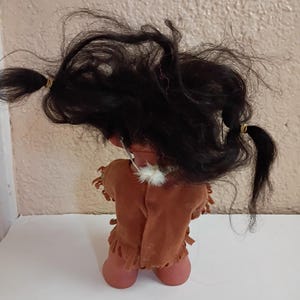 Puede incluir: Una mu&ntilde;eca vintage con cabello oscuro peinado en dos coletas. La mu&ntilde;eca lleva un chaleco marr&oacute;n tipo ante con flecos y un collar de plumas blancas. La piel de la mu&ntilde;eca es de color melocot&oacute;n claro.