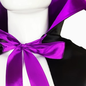 May include: A black satin cape with a purple satin lining and a purple satin bow tie. The cape has a stand-up collar.