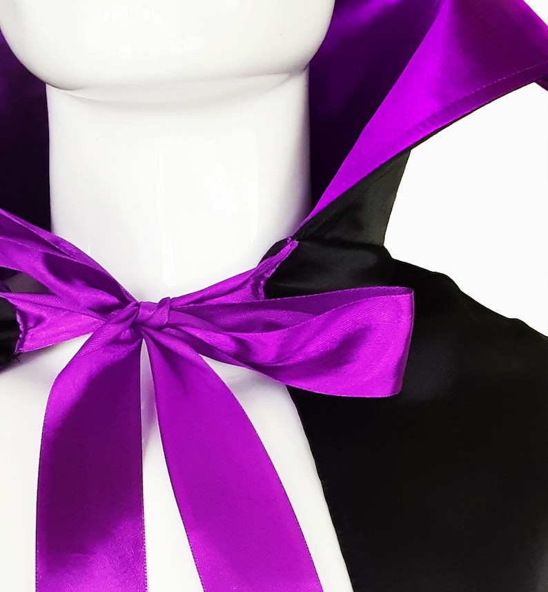 May include: A black satin cape with a purple satin lining and a purple satin bow tie. The cape has a stand-up collar.