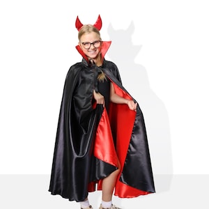 May include: A young person dressed as a devil for Halloween. They are wearing a black cape with a red lining and a red devil horn headband.