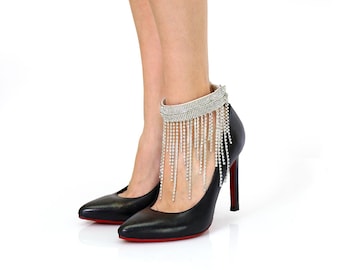 May include: A pair of black high-heeled shoes with a silver rhinestone ankle bracelet featuring a fringe design.