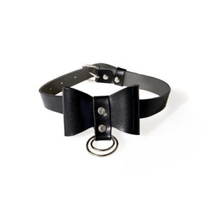 May include: Black leather choker with a bow and a silver ring. The bow has two silver studs.