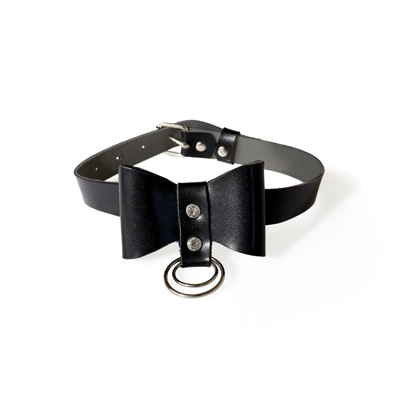May include: Black leather choker with a bow and a silver ring. The bow has two silver studs.
