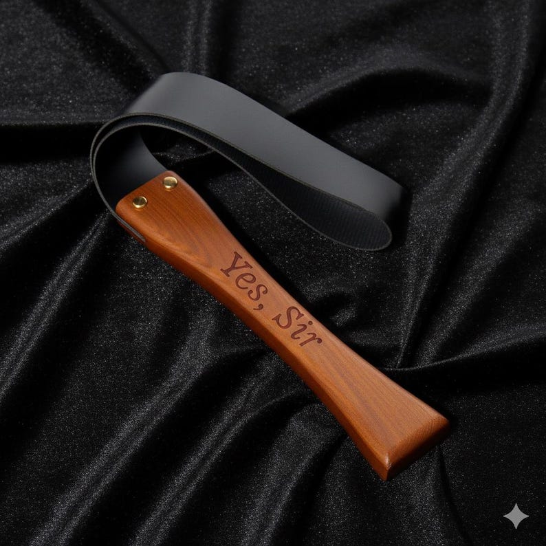 May include: A black leather flogger with a wooden handle. The handle is engraved with the words "Yes, Sir". The flogger is made of black leather and wood.