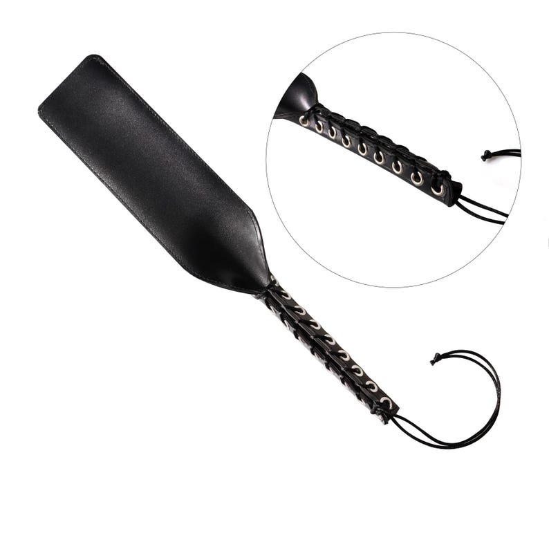 May include: A black leather paddle with a braided handle and silver metal accents. The handle is tied with a black cord.