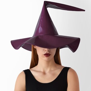 May include: A purple witch hat with a tall, pointed crown and a wide brim. The hat has a glossy finish and a curved brim.