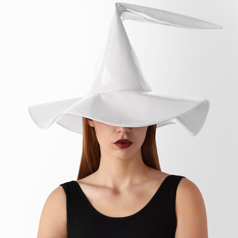 May include: A white witch hat with a long, pointed crown and a wide brim. The hat is made of a shiny, glossy material.