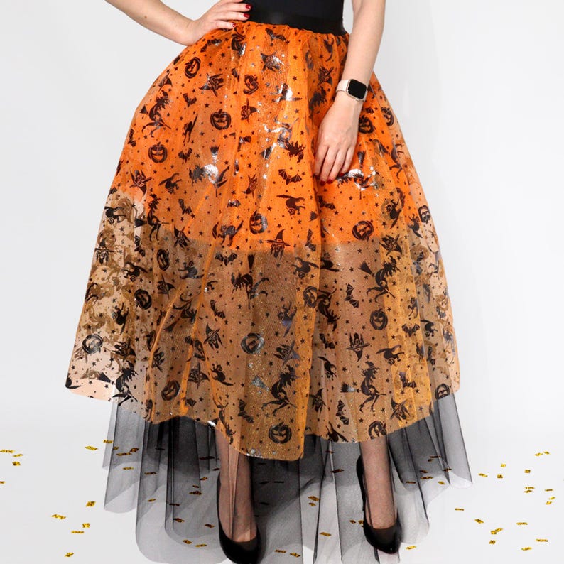 May include: A Halloween-themed skirt with an orange and black color scheme. The skirt features a layered design with a black tulle underskirt and an overlay adorned with Halloween-themed icons like bats, pumpkins, and witches. The skirt is worn with black heels.