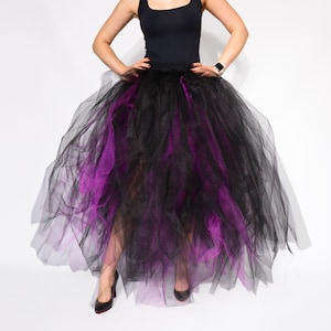May include: A black and purple tulle skirt. The skirt is layered, with black tulle on top and purple tulle peeking through. The skirt is paired with a black tank top and black heels. The skirt is full and flowing.