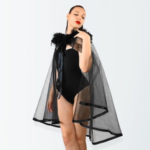 May include: A black sheer cape with a black feather trim collar and black satin ribbon ties. The cape has a layered design with multiple tiers of fabric.