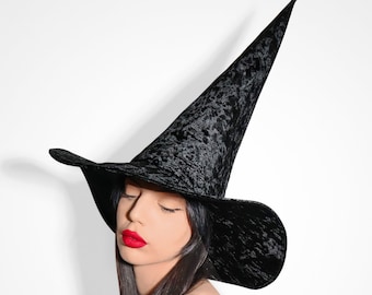 May include: A black velvet witch hat with a wide brim and a tall pointed crown. The hat is worn by a person with long dark hair and red lipstick.