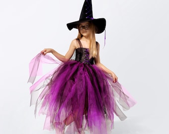 May include: A young girl dressed as a witch for Halloween. She is wearing a purple and black tulle dress with a black witch hat and glasses.