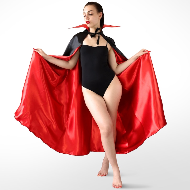 May include: A woman wearing a black bodysuit and a red satin cape with a black velvet collar. The cape is flowing behind her.