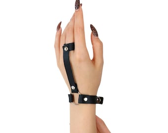 May include: Black leather finger ring with a metal ring and a strap that extends to the wrist. The ring is worn on the index finger.