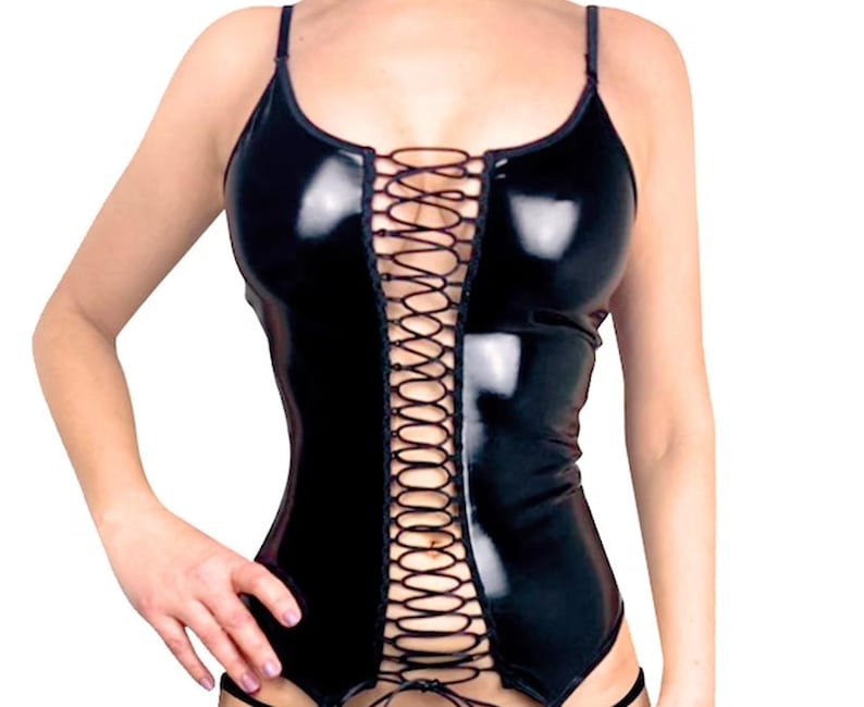 Op de afbeelding: Zwarte, glanzende corset-achtige top met spaghettibandjes en een veter aan de voorkant. De top heeft een getailleerd silhouet en is gemaakt van glanzend materiaal. Het ontwerp heeft een lage halslijn en een gedetailleerd vetersluitingspatroon.