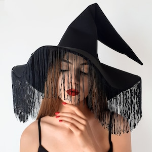 May include: A black witch hat with a wide brim and long fringe. The hat is made of felt and has a tall, pointed crown.
