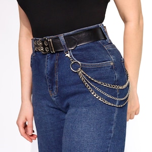 May include: A black leather belt with silver buckle and grommets, worn with blue jeans and a silver chain attached to the belt loop.