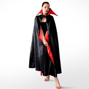 May include: A black satin cape with a red satin lining and a red velvet collar. The cape is worn by a person with red lipstick and a black dress.