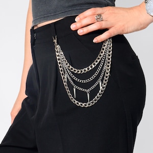 May include: Silver multi-chain pants chain with spike charms attached to a black pair of pants. The chain is attached to the pants with a silver clasp. The pants are high-waisted.