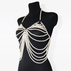 K&ouml;nnte beinhalten: Eine wei&szlig;e Perlen-K&ouml;rperkette mit einem zarten Ketten-Design. Die Kette besteht aus mehreren Perlenstr&auml;ngen und hat einen Halterneck-Stil.