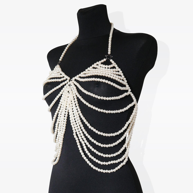 K&ouml;nnte beinhalten: Eine wei&szlig;e Perlen-K&ouml;rperkette mit einem zarten Ketten-Design. Die Kette besteht aus mehreren Perlenstr&auml;ngen und hat einen Halterneck-Stil.