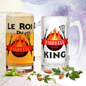 May include: Two clear glass beer mugs with handles. One mug says "Le Roi du Barbecue" with a red banner and a grill with flames. The other mug says "Barbecue King" with a red banner and a grill with flames.