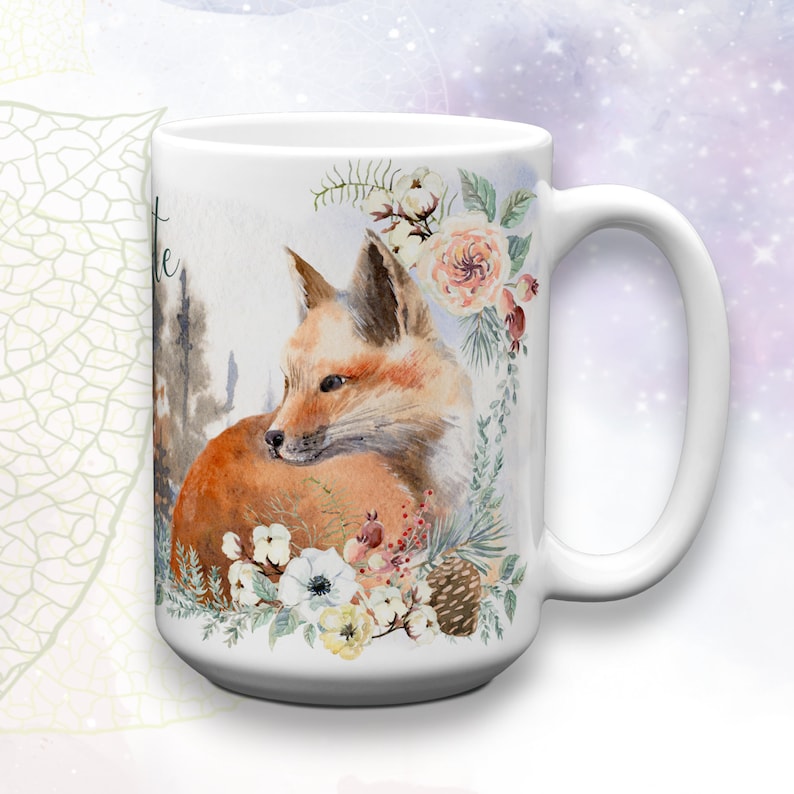 May include: White ceramic coffee mug with a watercolor illustration of a fox curled up with a floral arrangement. The flowers are white, pink, and yellow. The fox is orange and brown.