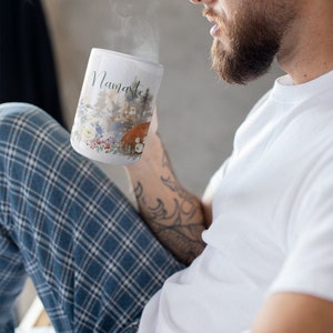 May include: A white ceramic mug with a watercolor design of a forest scene and the word "Namaste" printed on the front. The mug is filled with a hot beverage and steam is rising from the top.