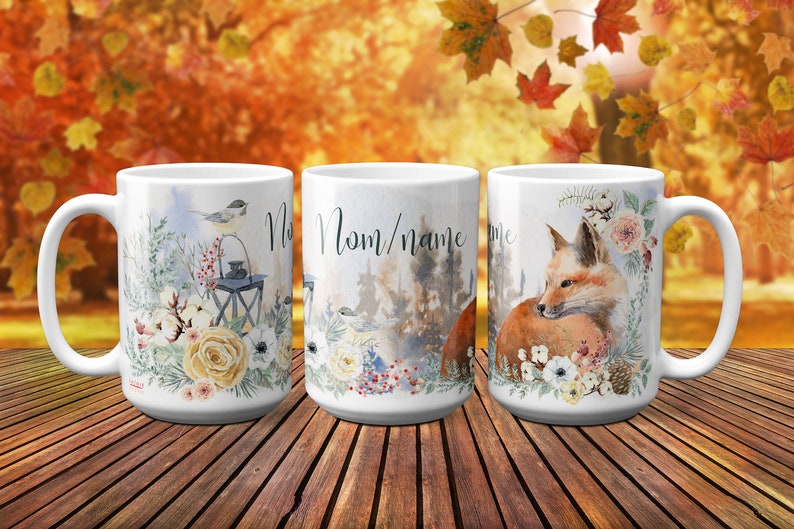 May include: Three white ceramic mugs with different designs. The first mug features a bird perched on a lantern with floral accents. The second mug has a forest scene with the text "Mom/name". The third mug features a fox curled up with floral accents.