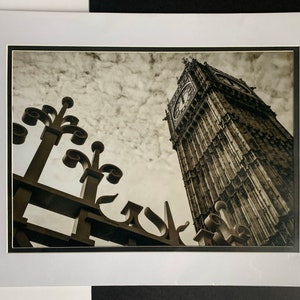 May include: A black and white photograph of Big Ben in London, England. The clock tower is seen from a low angle, with the top of the tower visible in the upper right corner of the image. The clock face is visible, and the hands are pointing to the time. The image is taken from a low angle, and the sky is visible in the background.