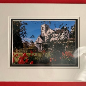 May include: A framed photograph of a white church with a clock tower, surrounded by a lush green lawn with red tulips in the foreground.