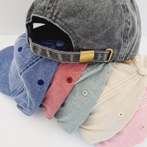 May include: Five denim baseball caps stacked on top of each other. The caps are in various shades of blue, pink, beige, and grey.