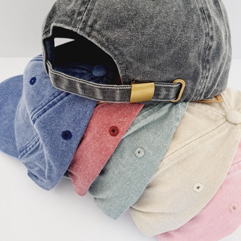 May include: Five denim baseball caps stacked on top of each other. The caps are in various shades of blue, pink, beige, and grey.
