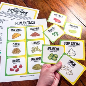 May include: A set of Human Taco game cards and instructions. The cards feature illustrations of taco ingredients like taco shells, meat, cheese, lettuce, tomato, guacamole, hot sauce, cilantro, lime juice, sour cream, jalapeño, and onion. The game is designed for group play.