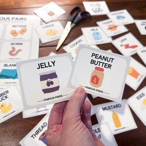 Peut inclure: Deux cartes blanches avec des illustrations d'un pot de confiture et d'un pot de beurre de cacahuètes. Les cartes font partie d'un jeu appelé "Famous Pairs".