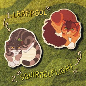 Op de afbeelding: Twee houten kattenfiguren, een bruin en grijs met een groen blad op zijn kop, en de andere oranje en bruin. De figuren zijn gelabeld "1. Leafpool" en "2. Squirrelflight".