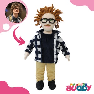May include: A plush doll with brown curly hair, wearing a blue and white plaid shirt over a navy blue shirt, khaki pants, and black shoes. The doll is wearing glasses and has a mustache.