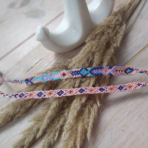 Könnte beinhalten: Zwei Freundschaftsarmbänder mit einem geometrischen Muster in Rosa-, Blau- und Orangetönen.