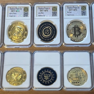 Może przedstawiać: Dziesięć złotych monet replik w ochronnych etui. Monety przedstawiają różne wzory, w tym lwa, postać, symbol Bitcoina i czaszkę. Każde etui ma etykietę z tekstem, w tym "Replica Props by UNITY ARTS."