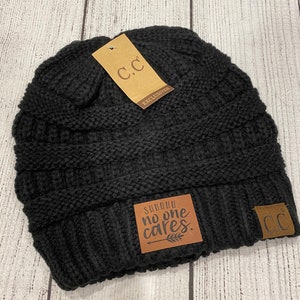 May include: Black knit beanie with a brown leather patch that says "Summer. No one cares." and a brown leather tag that says "C.C. Exclusives".