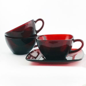 May include: Three red glass teacups and a matching saucer. The cups are stacked on top of each other, with the saucer in front of them.