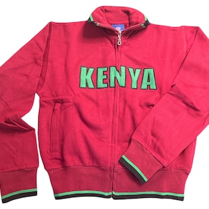 May include: Red zippered sweatshirt with green and black trim. The sweatshirt has the word "KENYA" printed on the front in green letters with a black outline.