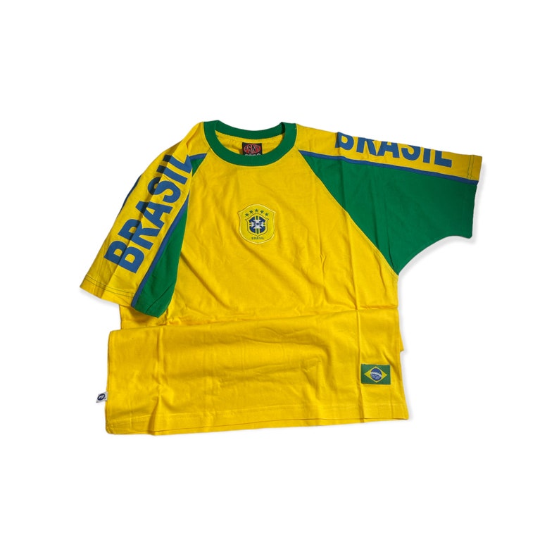 May include: Yellow and green t-shirt with a blue "BRASIL" print on the sleeve and a small embroidered crest on the front. The shirt has a raglan sleeve design.