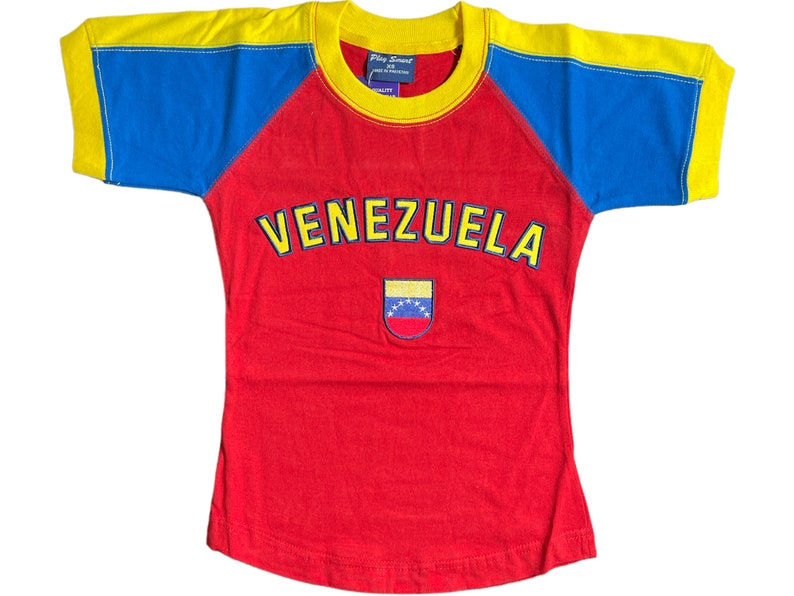 May include: A red, yellow, and blue t-shirt with a baseball style design. The shirt has the word "VENEZUELA" in yellow letters on the front and a small embroidered Venezuelan flag.