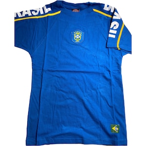 May include: Blue t-shirt with a yellow and white "BRASIL" graphic on the sleeve and a yellow and green crest with "BRASIL" text on the front.